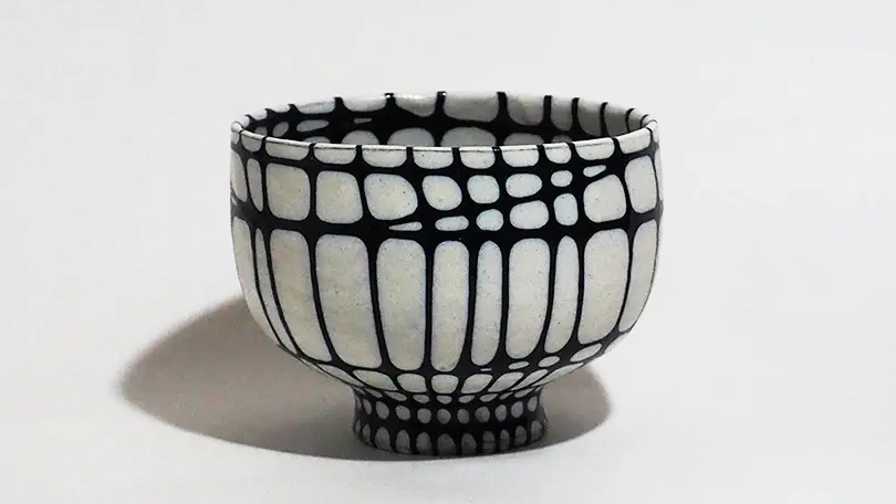 青色の網目状の紋様が付された茶碗、網目は、円周方向と軸方向の両方に複数施されており、軸方向の網目は僅かに弧を描きつつも、ほぼ等間隔であるが、円周方向の網目は、上部がより密接しており、下部の方が感覚が開いている、茶碗全体が膨らみのある形状をしている。