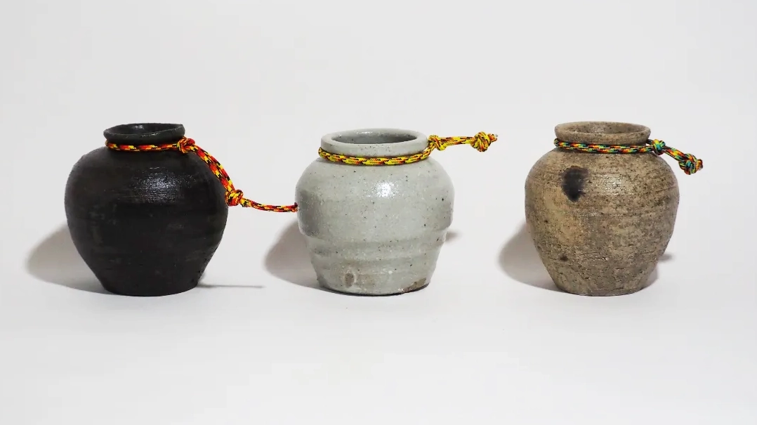 黒、灰白色、灰色の3点で構成された小型の壺作品。壺の首部分には、腰から吊るして持ち歩くことを想起させる紐状の装飾が取り付けられている。作品により、表面には焼成による自然な色むらや質感が見られ、素朴で使い込まれた雰囲気を持つ。実用品と装身具の中間のような、風変わりで遊び心のある印象を与える作品群。